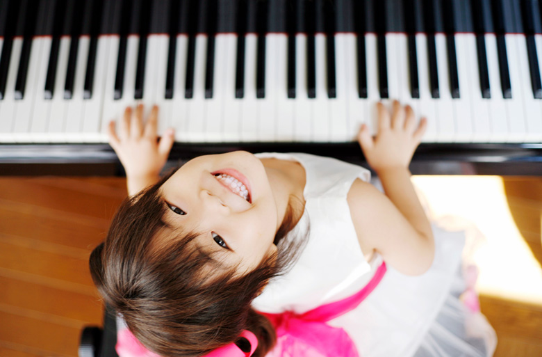 ピアノを弾きながら笑顔で見上げる女の子の写真